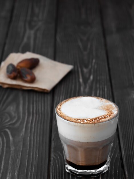 Tazza di caffè di vetro con latte su una superficie di legno scura