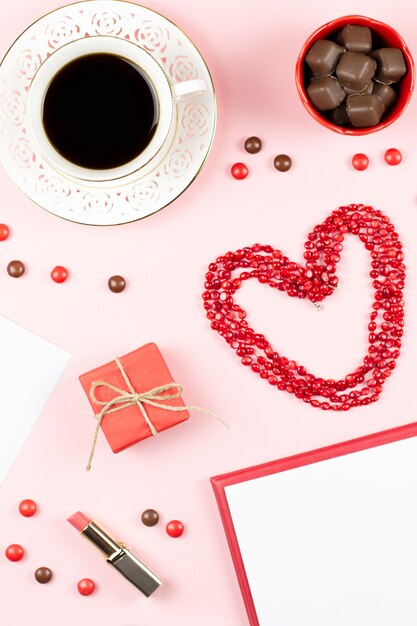 Tazza di caffè, dolci, rossetto, a forma di cuore e giftbox su sfondo rosa. Concetto di festa della donna piatta laici.