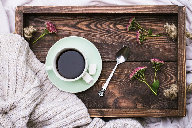 Tazza di caffè e candela sul vassoio da portata in legno rustico e maglione di lana caldo per maglieria