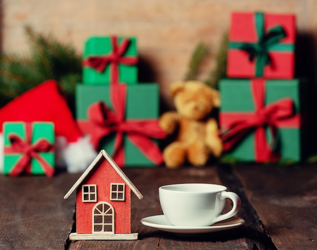 Tazza di caffè e casa giocattolo sul tavolo di legno accanto ai regali di Natale