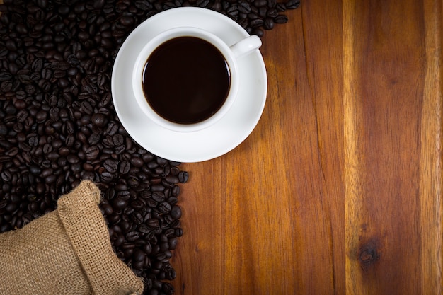 Tazza di caffè e chicchi di caffè in un sacco su legno