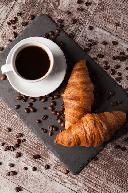 Tazza di caffè e chicchi di caffè sparsi con croissant freschi. Dolce delizioso.