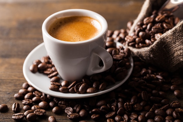 Tazza di caffè e chicchi di caffè sparsi su fondo di legno