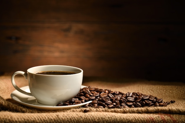 Tazza di caffè e chicchi di caffè sul sacco di iuta su fondo in legno vecchio