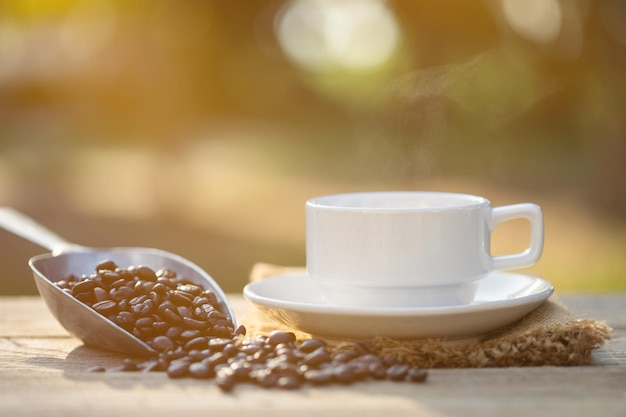 Tazza di caffè e chicchi di caffè sulla tavola di legno all'aperto alla luce del sole del mattino e sullo sfondo del bokeh