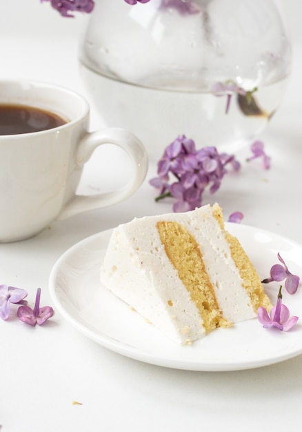 Tazza di caffè e corna di torta da natura morta con un mazzo di lillà su un tavolo bianco una tazza di caffè un piatto con un pezzo di torta Giornata internazionale della donna 8 marzo