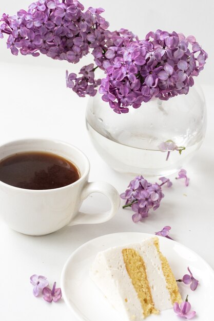 Tazza di caffè e corna di torta di natura morta con un mazzo di lillà su un tavolo bianco, una tazza di caffè, un piatto con un pezzo di torta. Giornata internazionale della donna, 8 marzo
