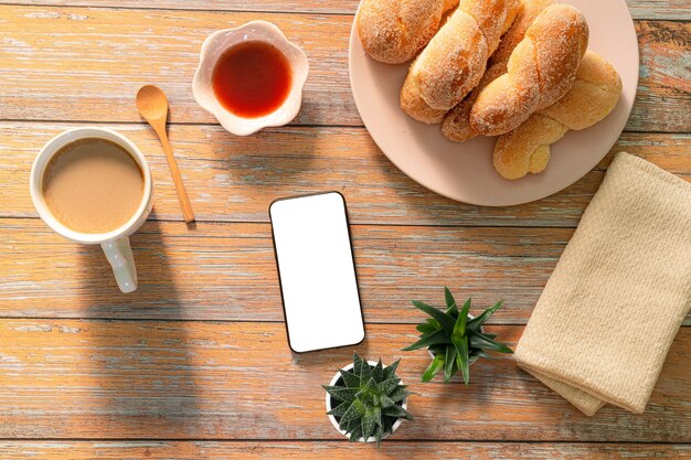 Tazza di caffè e croissant appena sfornati auricolari smart phone su sfondo di legno Vista dall'alto