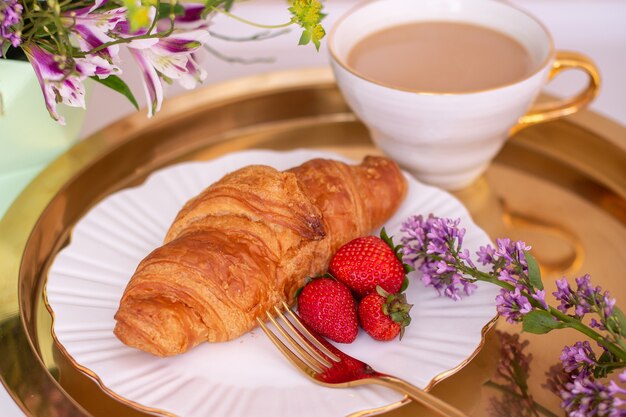 Tazza di caffè e croissant con fragole fresche su piatto dorato