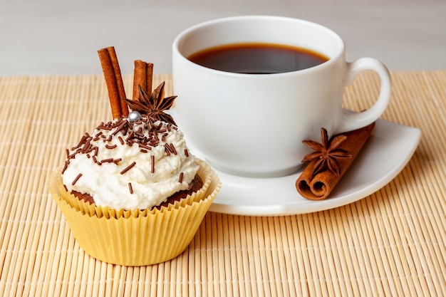 Tazza di caffè e cupcake con crema e spolverini decorativi di cioccolato bastoncini di cannella e anice