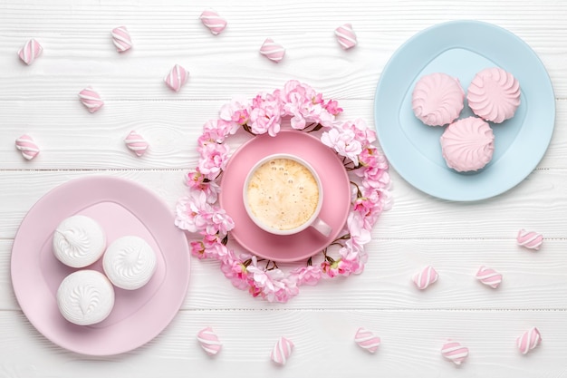 Tazza di caffè e fiori primaverili Dessert al mattino per colazione vista dall'alto Fiore di ciliegio su un tavolo di legno bianco Design piatto laici Carta a colori pastello Sfondo di cibi e bevande Decorazioni floreali