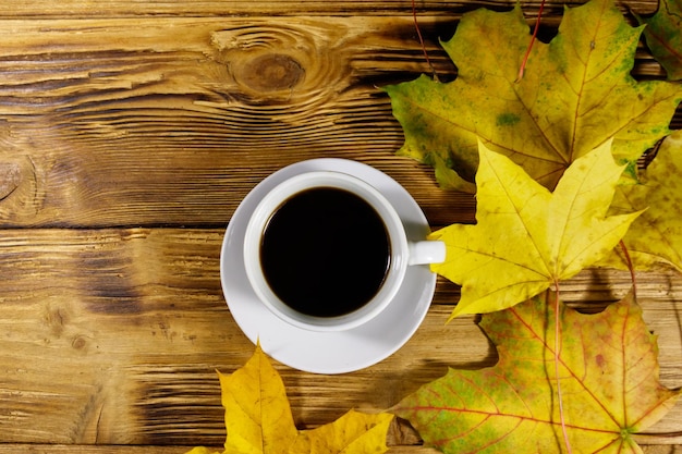 Tazza di caffè e foglie d'acero autunnali su un tavolo di legno Vista dall'alto Concetto di autunno