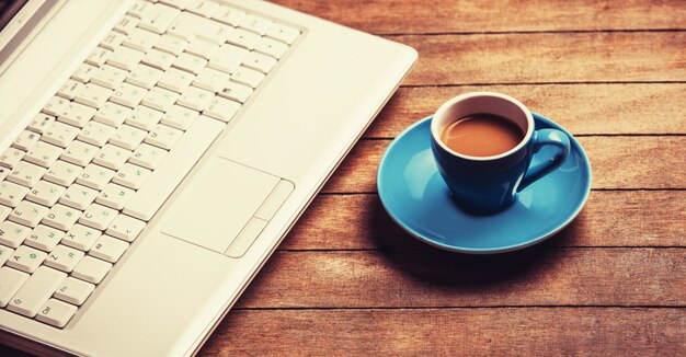 Tazza di caffè e laptop sul tavolo di legno.