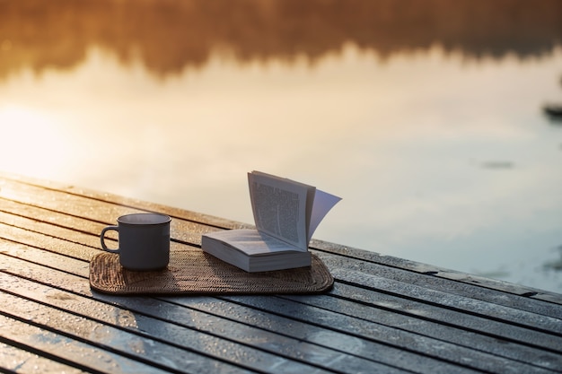 Tazza di caffè e libro sul molo di legno sul lago estivo