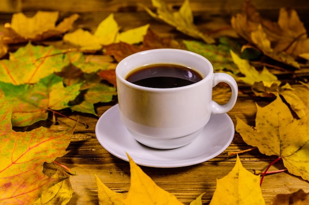 Tazza di caffè e mucchio di foglie di acero gialle su un tavolo di legno