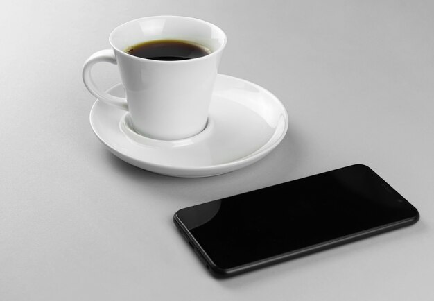 Tazza di caffè e smartphone su uno sfondo grigio