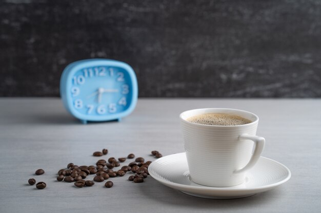 Tazza di caffè e sveglia blu sul tavolo bianco.