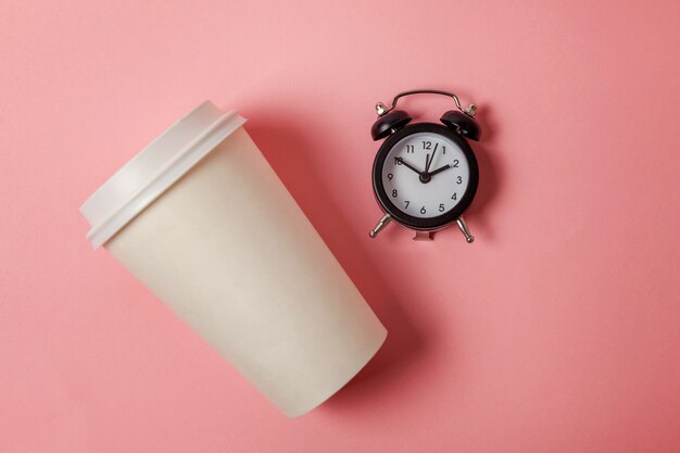 Tazza di caffè e sveglia di carta su fondo rosa