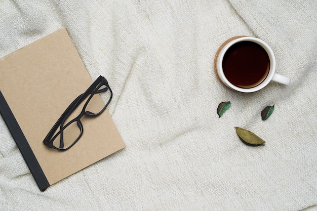 Tazza di caffè e taccuino con gli occhiali sulla priorità bassa marrone del filato.