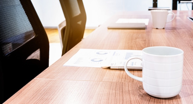 Tazza di caffè e taccuino sul tavolo con due poltrone nere nella sala riunioni