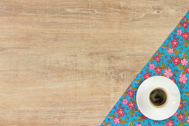 Tazza di caffè e tovagliolo di stoffa floreale su fondo di legno.