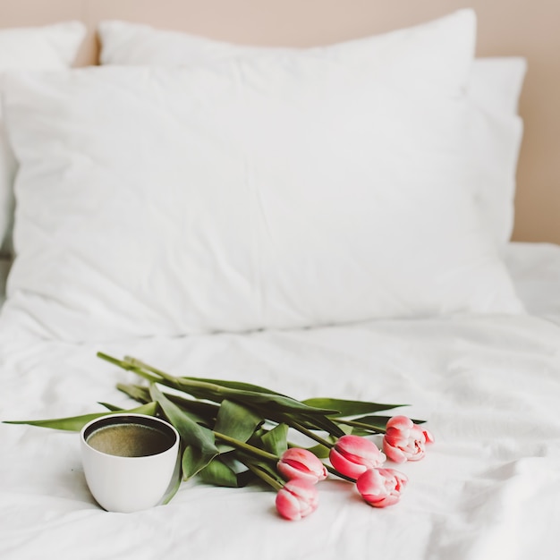 Tazza di caffè e tulipani a letto su lenzuola bianche