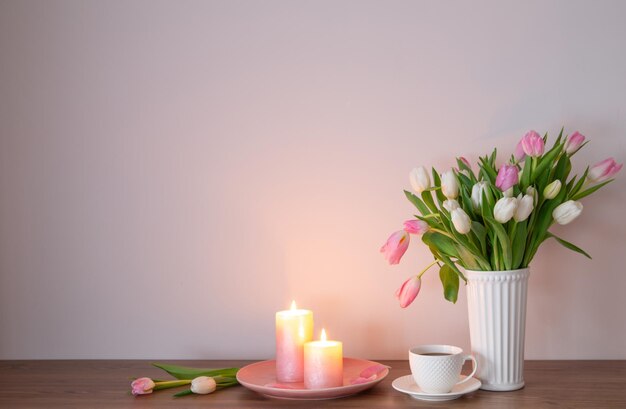 tazza di caffè e tulipani primaverili in vaso con candele accese su uno scaffale di legno