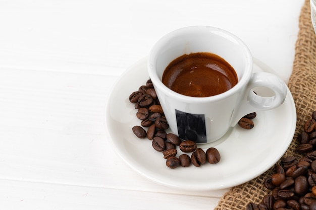 Tazza di caffè espresso e chicchi di caffè sulla superficie bianca