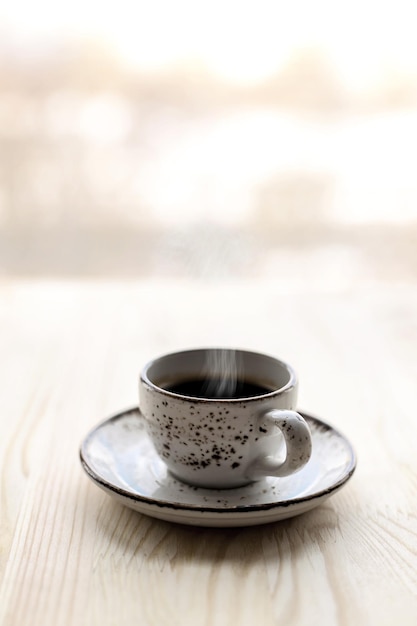 Tazza di caffè espresso sul piattino sul tavolo di legno vicino alla finestra sfocato sullo sfondo della città