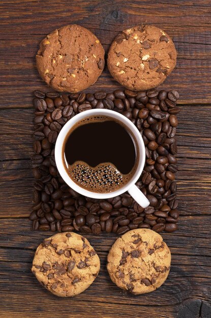 Tazza di caffè, fagioli a forma di quadrato e biscotti con cioccolato e noci su fondo di legno scuro, vista dall'alto