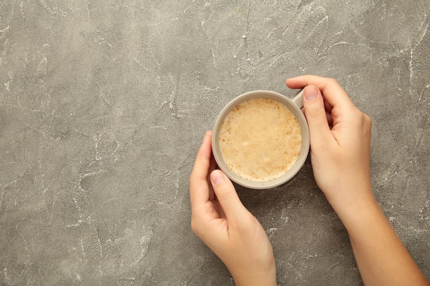 Tazza di caffè femminile della stretta della mano su fondo grigio concreto