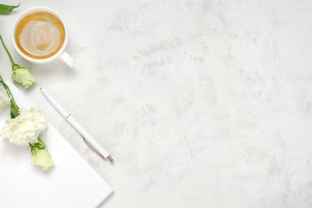 Tazza di caffè, fiori, taccuino e penna su priorità bassa concreta bianca con lo spazio della copia