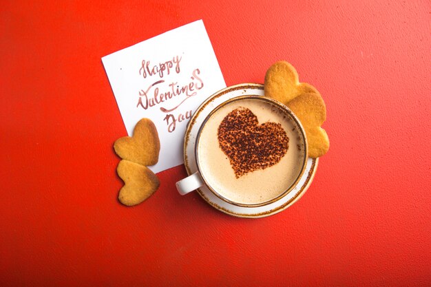 Tazza di caffè fresco con i biscotti del cuore sulla tavola rossa