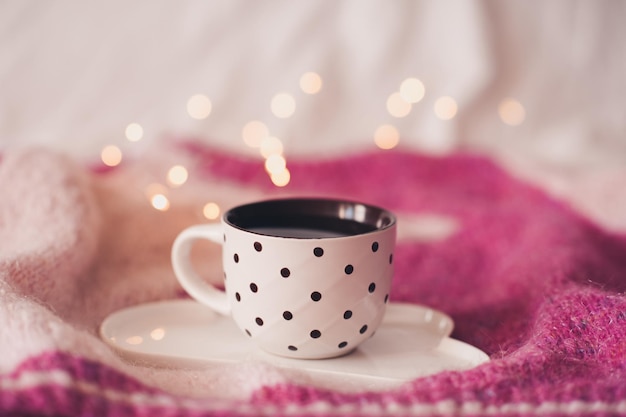 Tazza di caffè fresco sul vassoio sul maglione lavorato a maglia sopra le luci glowig da vicino. Buon giorno. Ora di colazione.