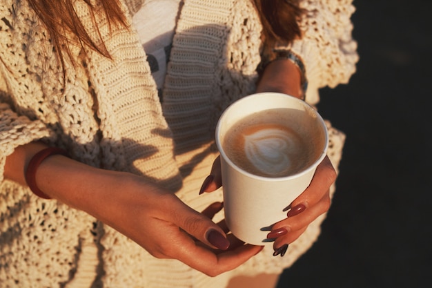 Tazza di caffè in mano. Le mani della donna che tengono la tazza di carta di un caffè.