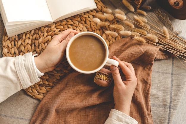 Tazza di caffè in mano vista dall'alto macarons e foto estetica del libro aperto