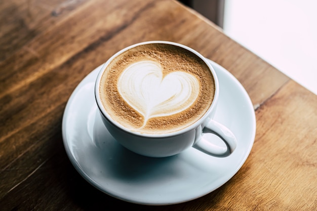 Tazza di caffè latte a forma di cuore su sfondo di legno vecchio alla luce del sole del mattino