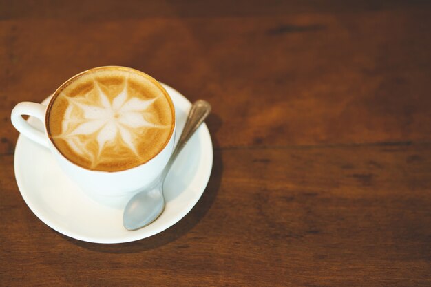 Tazza di caffè latte con forma di cuore e chicchi di caffè su fondo in legno vecchio