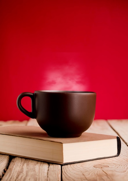 Tazza di caffè marrone con fumo sul libro di lettura tavolo in legno rustico sfondo rosso