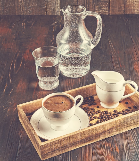 Tazza di caffè nero, chicchi di caffè e acqua in una scatola di legno, immagine tonica.