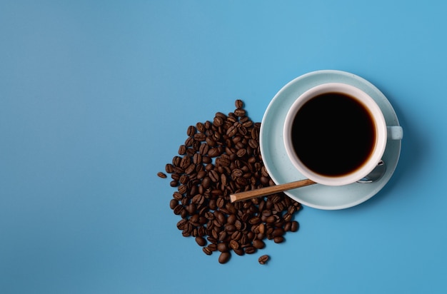 Tazza di caffè nero e chicchi di caffè su sfondo blu, copia spazio per il testo.