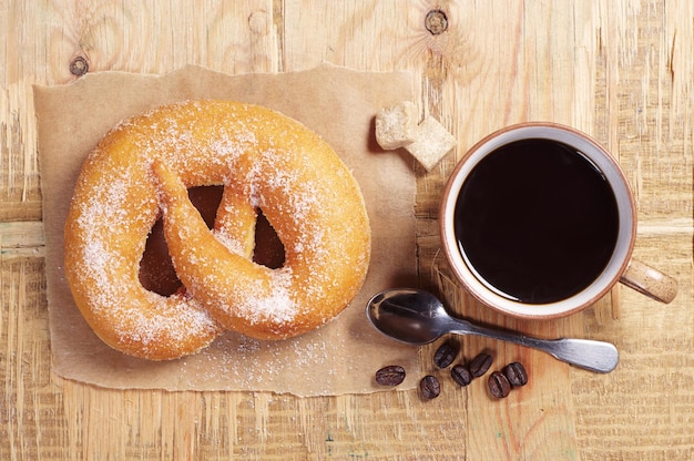 Tazza di caffè nero e panino intrecciato con zucchero sul vecchio tavolo di legno. Vista dall'alto