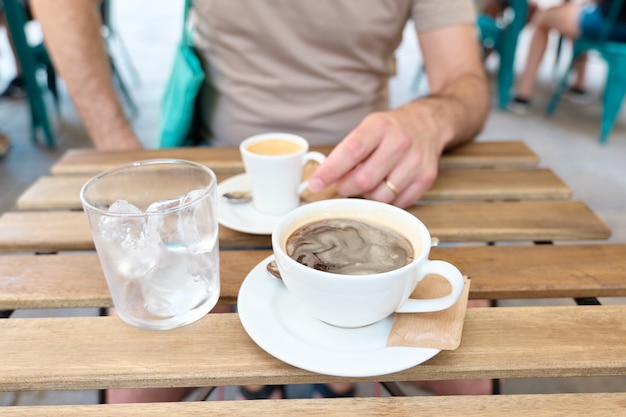 Tazza di caffè nero e un bicchiere con ghiaccio su un tavolo bar, all'aperto