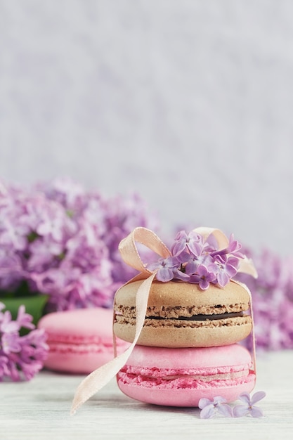 Tazza di caffè nero, fiori lilla e dolci amaretti francesi pastello sul tavolo in legno chiaro