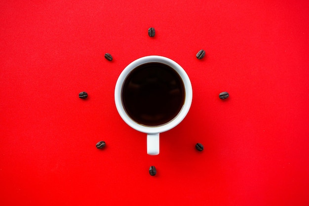Tazza di caffè nero su sfondo rosso con chicchi di caffè disposti a formare il quadrante dell'orologio