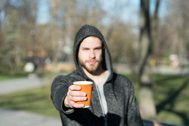 Tazza di caffè o tè in mano di uomo sfocato nel parco