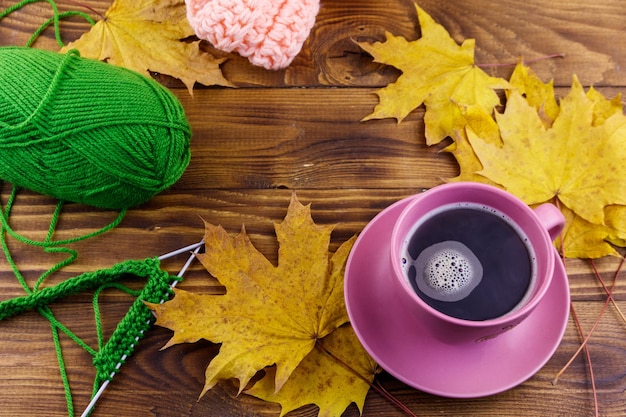 Tazza di caffè palla di filato sciarpa lavorata a maglia e foglie di acero gialle su tavola di legno Autunno ancora vita