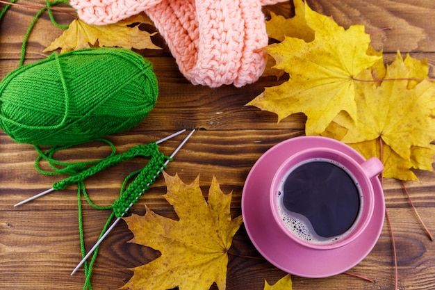 Tazza di caffè palla di filato sciarpa lavorata a maglia e foglie di acero gialle su tavola di legno Autunno ancora vita