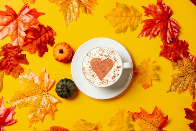 Tazza di caffè romantica e piccole zucche con foglie autunnali su sfondo giallo. Vista dall'alto