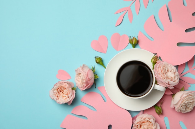 Tazza di caffè, rose e foglie di carta su sfondo blu, vista dall'alto